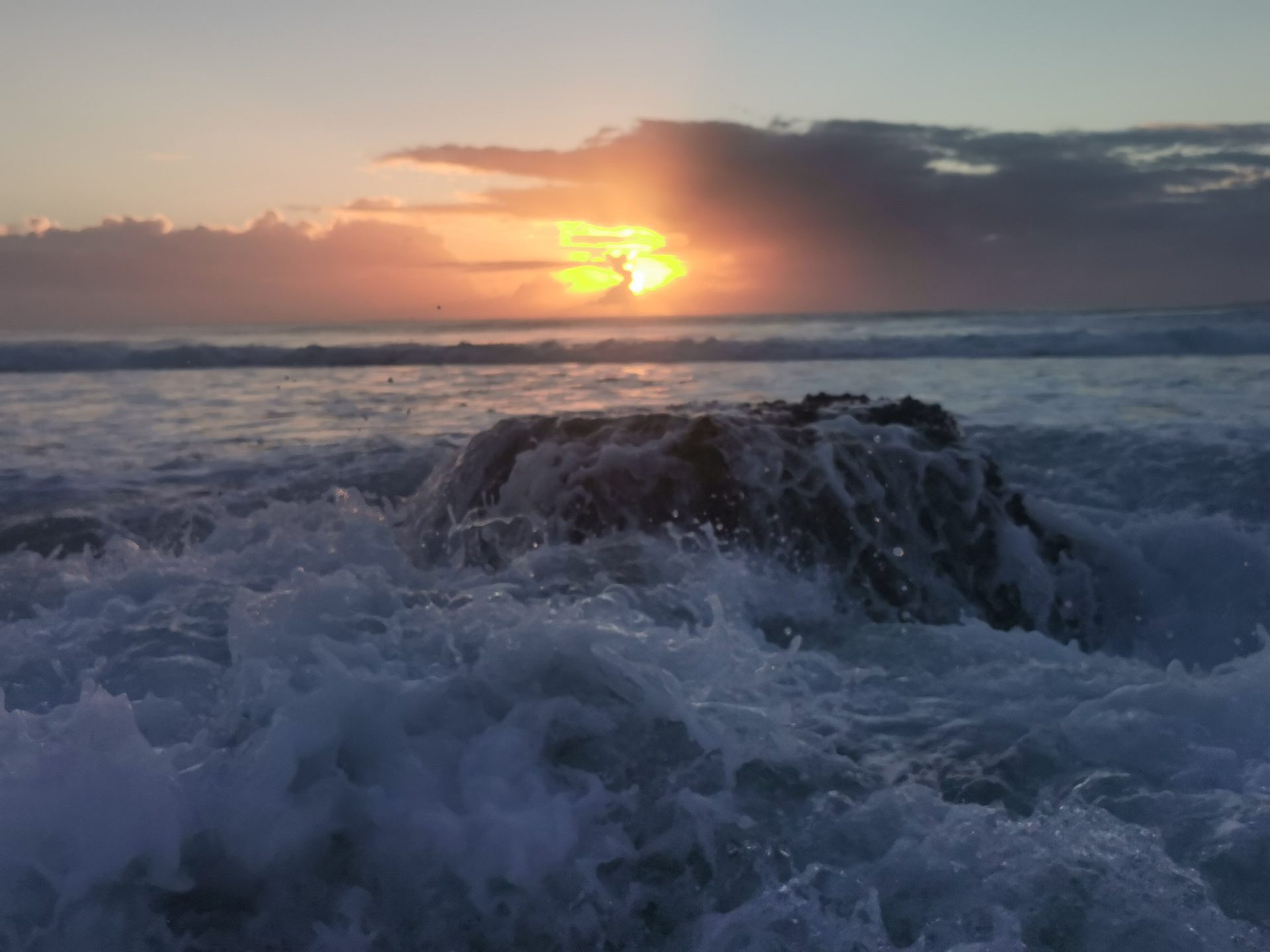Sunrise over a wave breaking on the beach